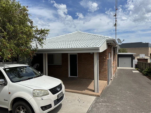 Brick house with a restored pale tile hip roof, carport and driveway.